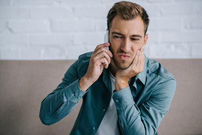 man on the phone holding his mouth due to tooth pain